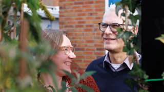 Twee mensen poseren samen buiten tussen planten en een bakstenen muur