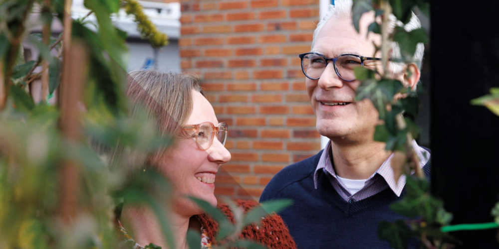 Twee mensen poseren samen buiten tussen planten en een bakstenen muur