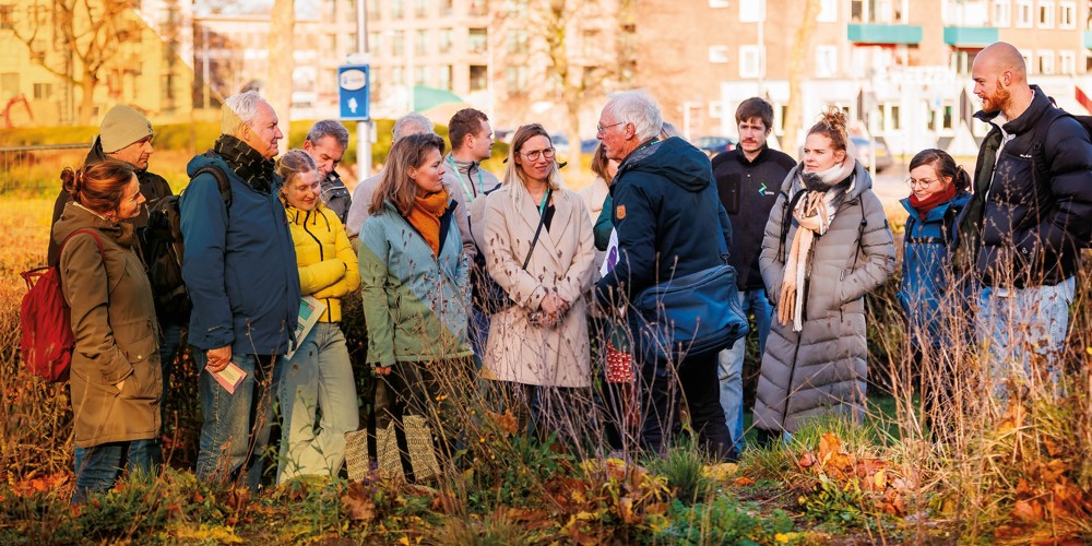 Groep mensen in een park luistert naar een spreker tijdens een excursie. De mensen dragen een dikke jas. Fotograaf: C Ewald Geerdink