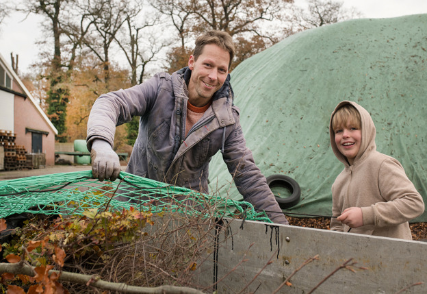 Man en kind laden jonge bomen op aanhanger op erf