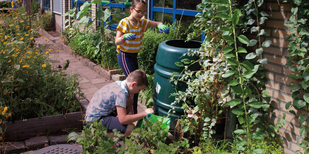 Twee kinderen verzorgen planten in een groene schooltuin naast een schoolgebouw