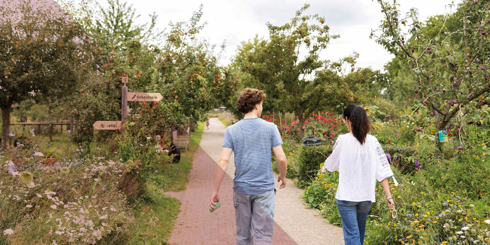 Twee mensen wandelen over een tuinpad tussen bloemen en struiken