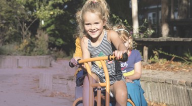 Kinderen rijden samen op een driewieler in een groene buitenruimte