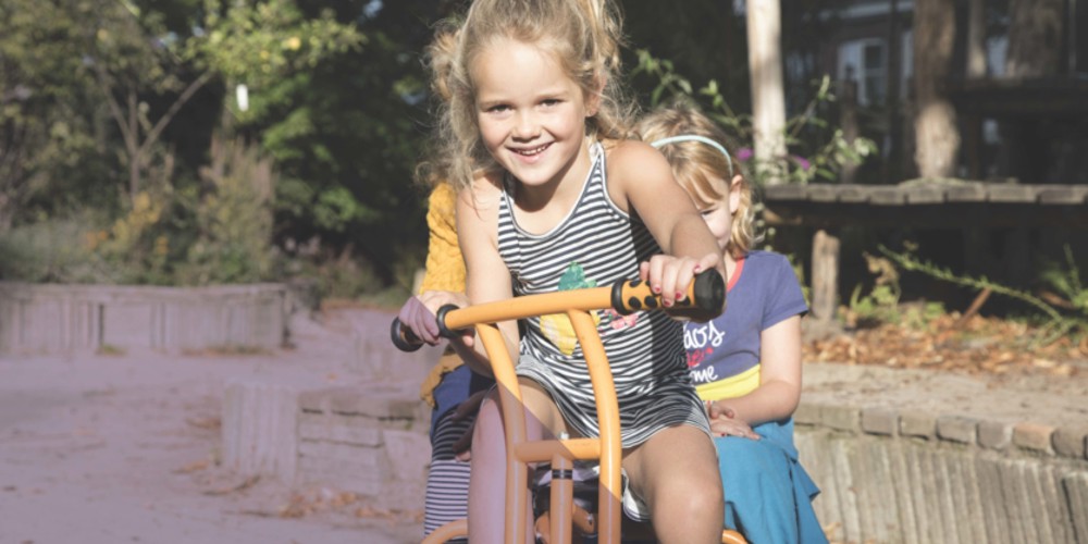 Kinderen rijden samen op een driewieler in een groene buitenruimte