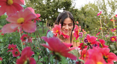 Vrouw glimlacht tussen felroze bloemen in een tuin op een zomerse dag.