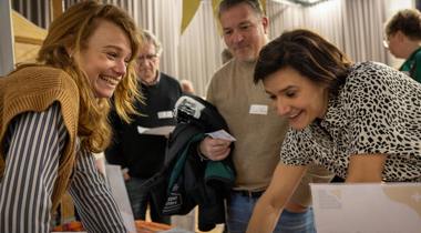 Twee vrouwen lachen en praten aan een informatiestand op Fondsen Festival