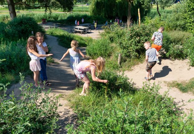 Kinderen die spelen in een speeltuin met veel lang gras en smalle zandpaden