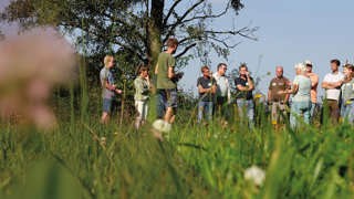 Groep mensen staat in een grasveld en luistert naar een spreker