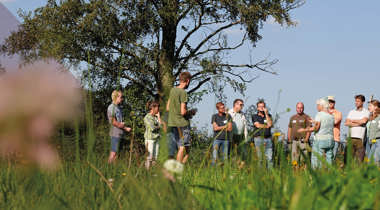 Groep mensen staat in een grasveld en luistert naar een spreker