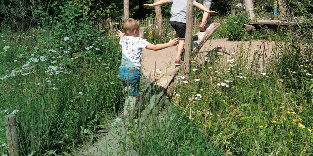 Drie kinderen spelen op houten structuren in een groene omgeving.
